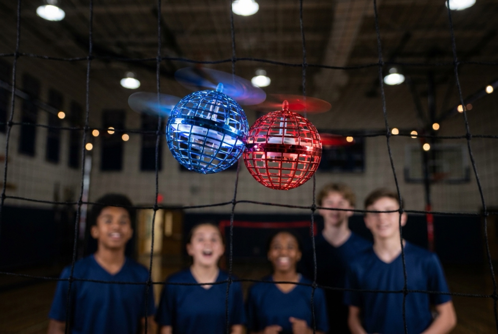 Two caged drones glowing red and blue meeting in mid-air inside the arena net